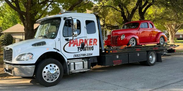 White tow truck carrying a red vintage car on its flatbed.