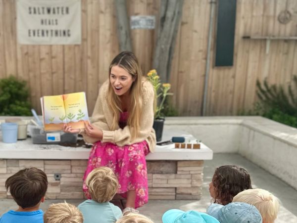 Woman reading a book to children outdoors.