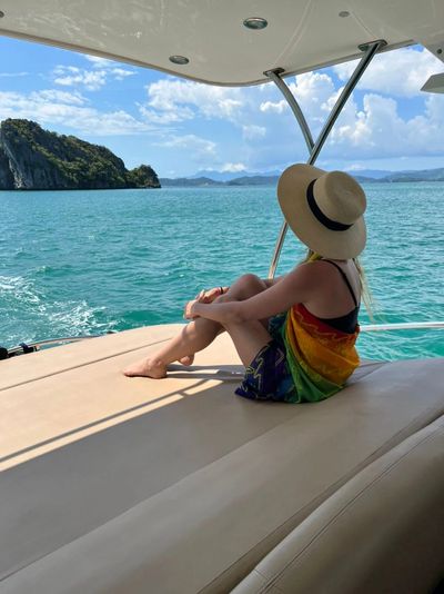 Woman in sunhat relaxing on a yacht, enjoying ocean views and scenic islands under a bright blue sky