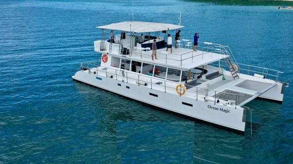 White catamaran Ocean Magic with guests on board, cruising on clear blue waters.