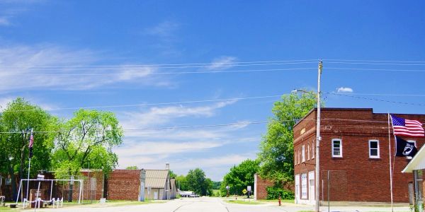 Small-town street with brick buildings and American flags under a clear blue sky.