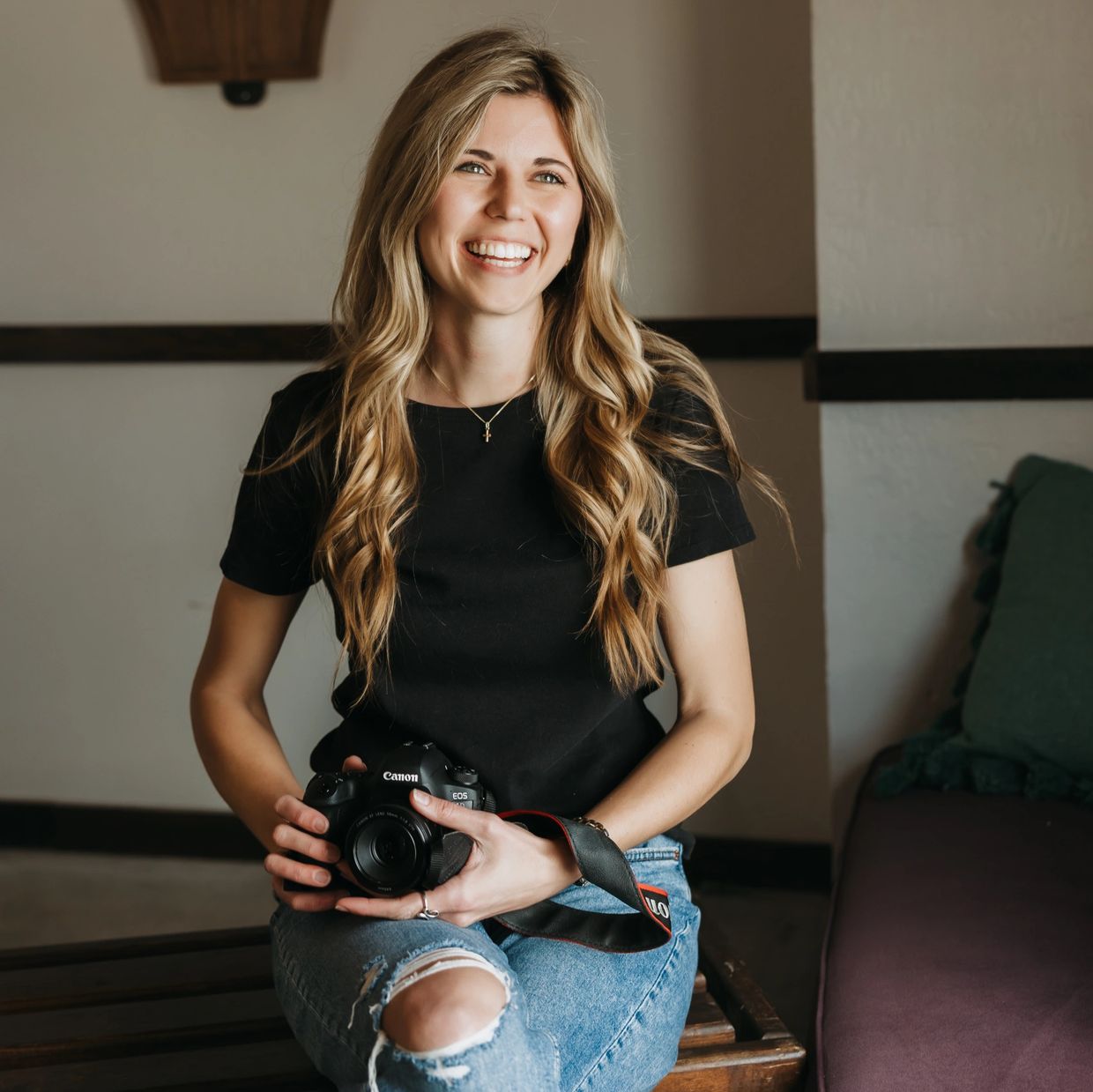 Young woman smiling while holding a Canon camera.