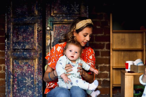 A woman in a red floral top holding a baby indoors.