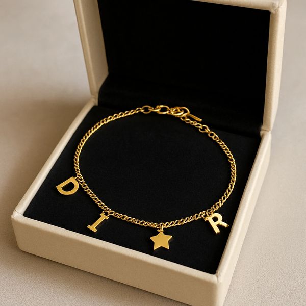 Gold charm bracelet with letters D, I, R and a star in a beige box.