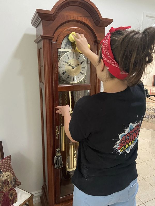 Person cleaning a wooden grandfather clock with a yellow cloth.