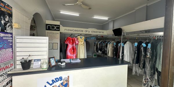 Interior of Newcastle Dry Cleaners with clothes hanging and counter.