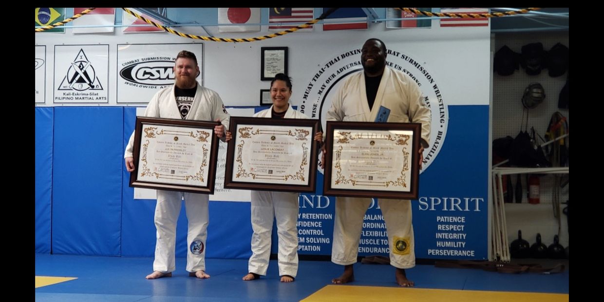 Three martial artists proudly holding framed certificates in a dojo.