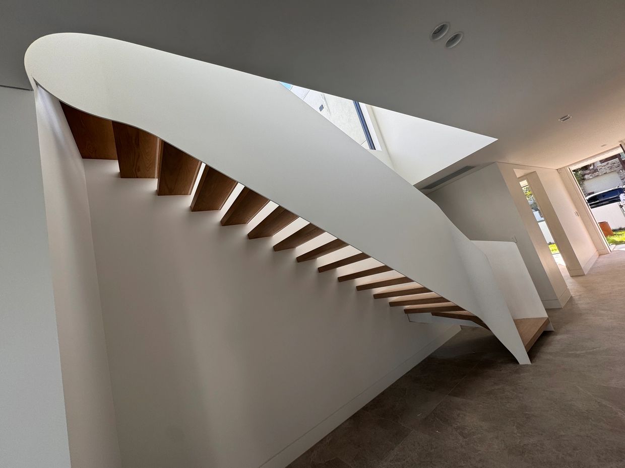 Modern floating staircase with wooden steps and white curved railing.