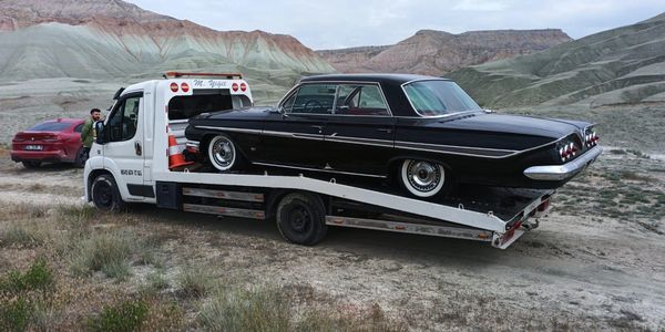 A vintage black car loaded on a white tow truck in a desert landscape.