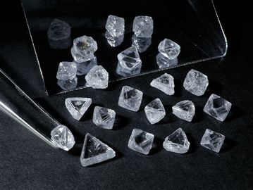 Collection of rough, uncut diamonds on a black surface with tweezers.