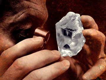 A person closely inspecting a large rough diamond with a jeweler's loupe.