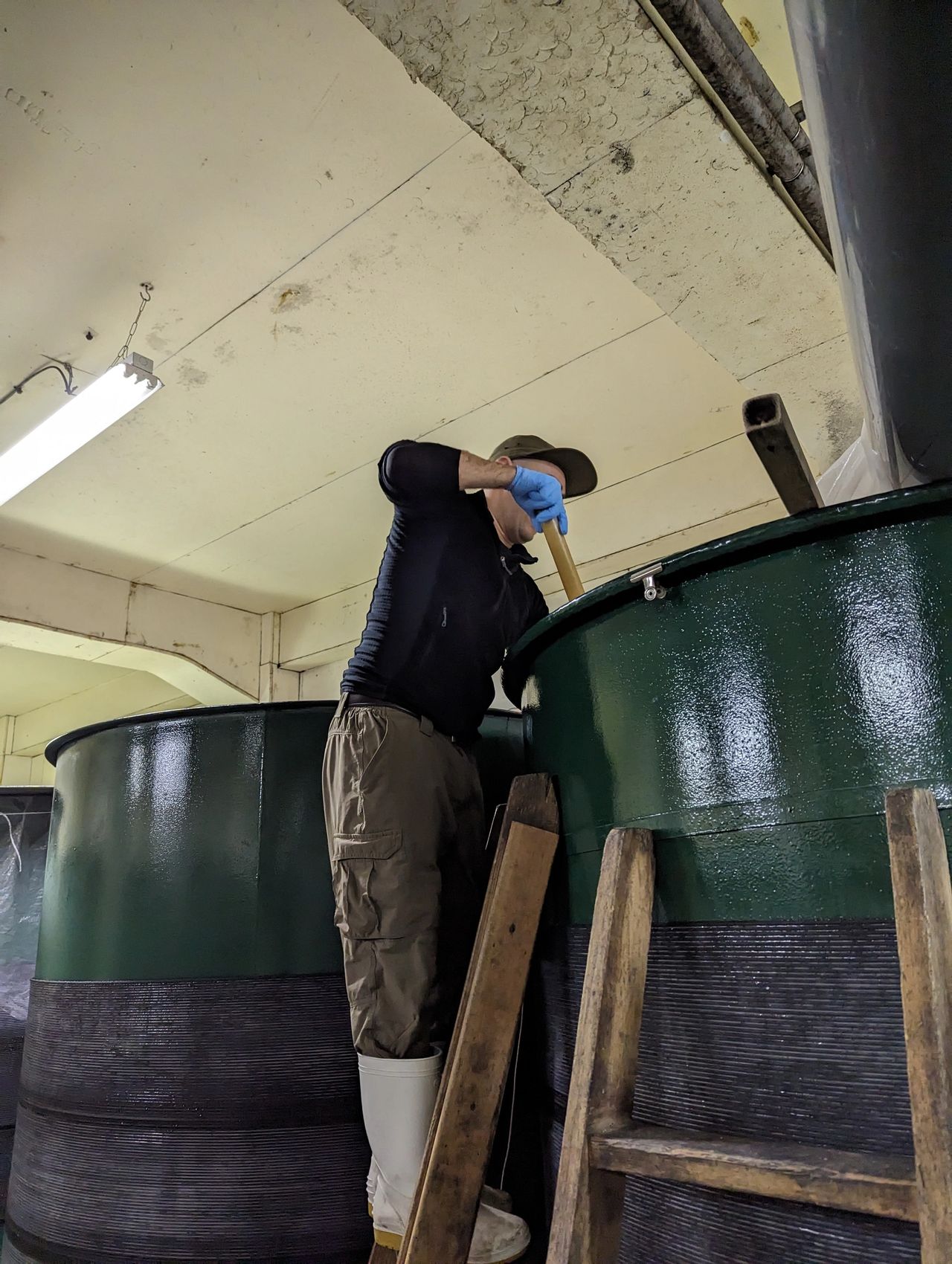 a man using a paddle to mix the moromi as part of the process of making Japanese sake