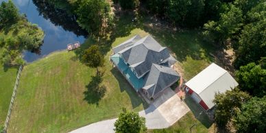 A house with a green roof near a pond and surrounded by trees.