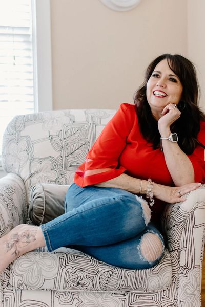 Woman in red top lounging on a patterned armchair, smiling.