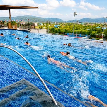 People swimming in an outdoor pool with a scenic backdrop.