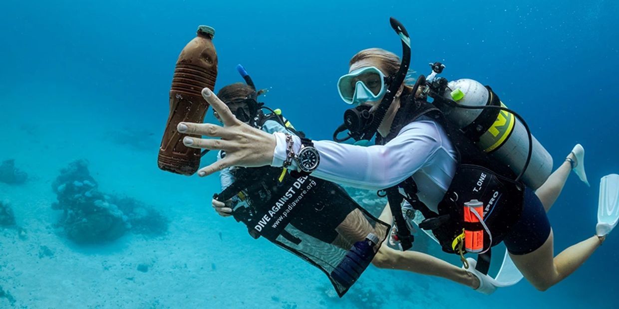 Two scuba divers underwater collecting a plastic bottle to protect the ocean.