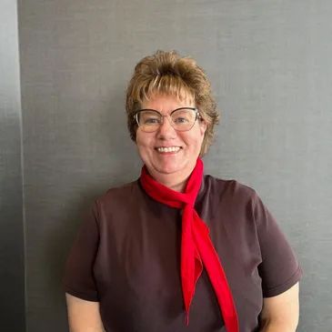 Smiling woman wearing glasses and a red scarf against a gray background.