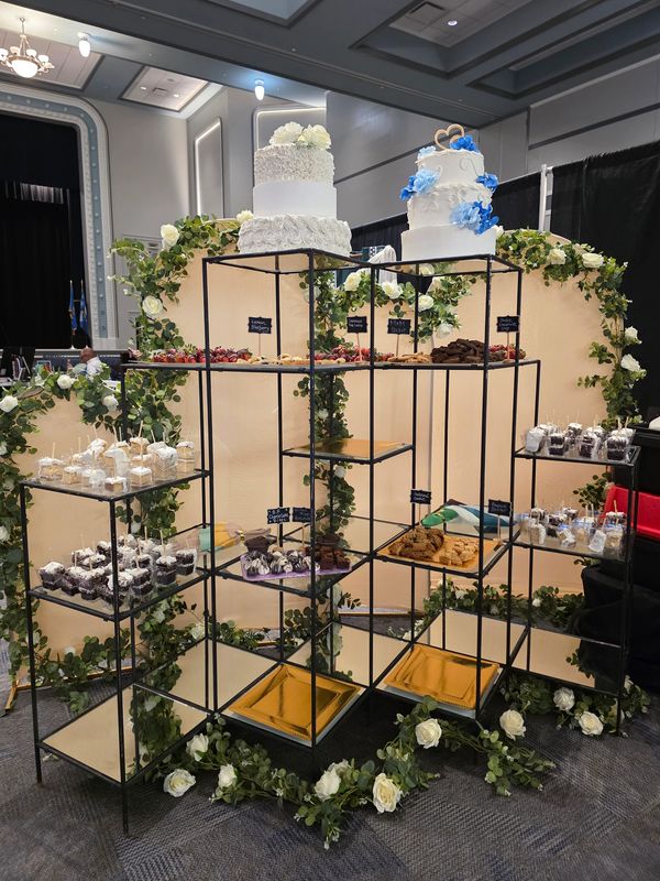 Elegant dessert display with cakes and treats decorated with flowers and greenery.