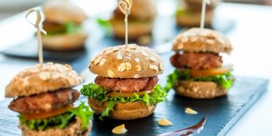 Three gourmet mini burgers with lettuce and tomato on a black slate.