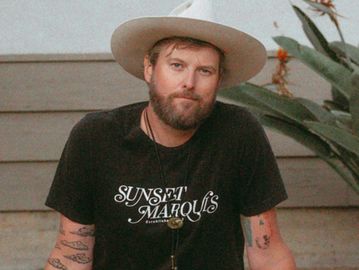 Man wearing a wide-brimmed hat and black Sunset Marquis t-shirt.