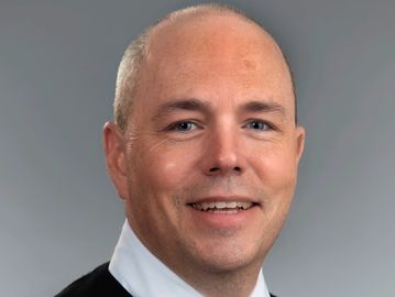 Smiling bald man in formal attire against a plain background.