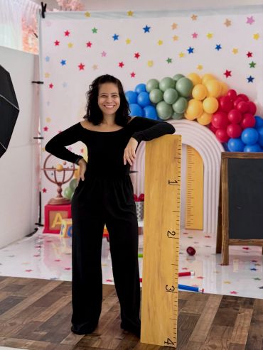 Woman standing next to a wooden height ruler in a colorful room.