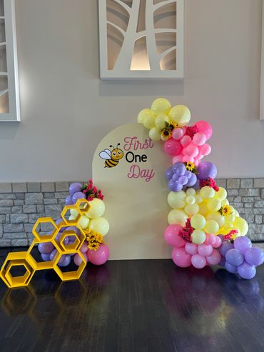 Pink, purple, and yellow balloon garland with florals, first birthday sign, and hexagon stand.