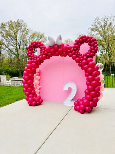 Pink Mickey Mouse balloon arch with light pink backdrop, number two marquee, and bow.