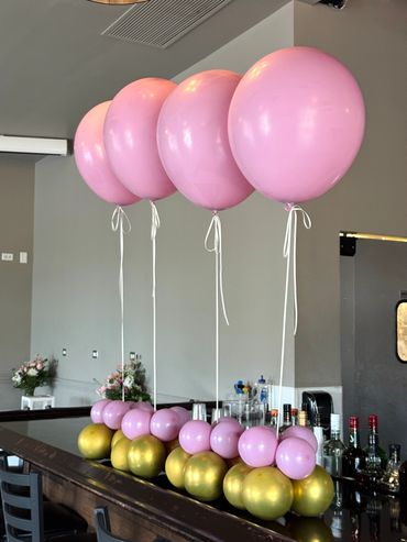 Elegant pink and gold balloon decorations lined up on a bar counter.