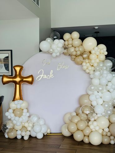 Round backdrop with balloon garland, balloon column with a cross topper balloon, and vinyl sign