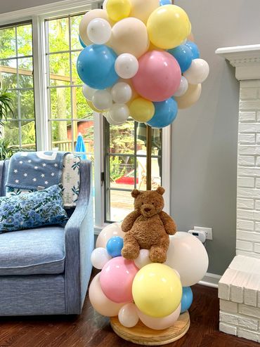 Colorful balloon arrangement with a teddy bear in a cozy living room.