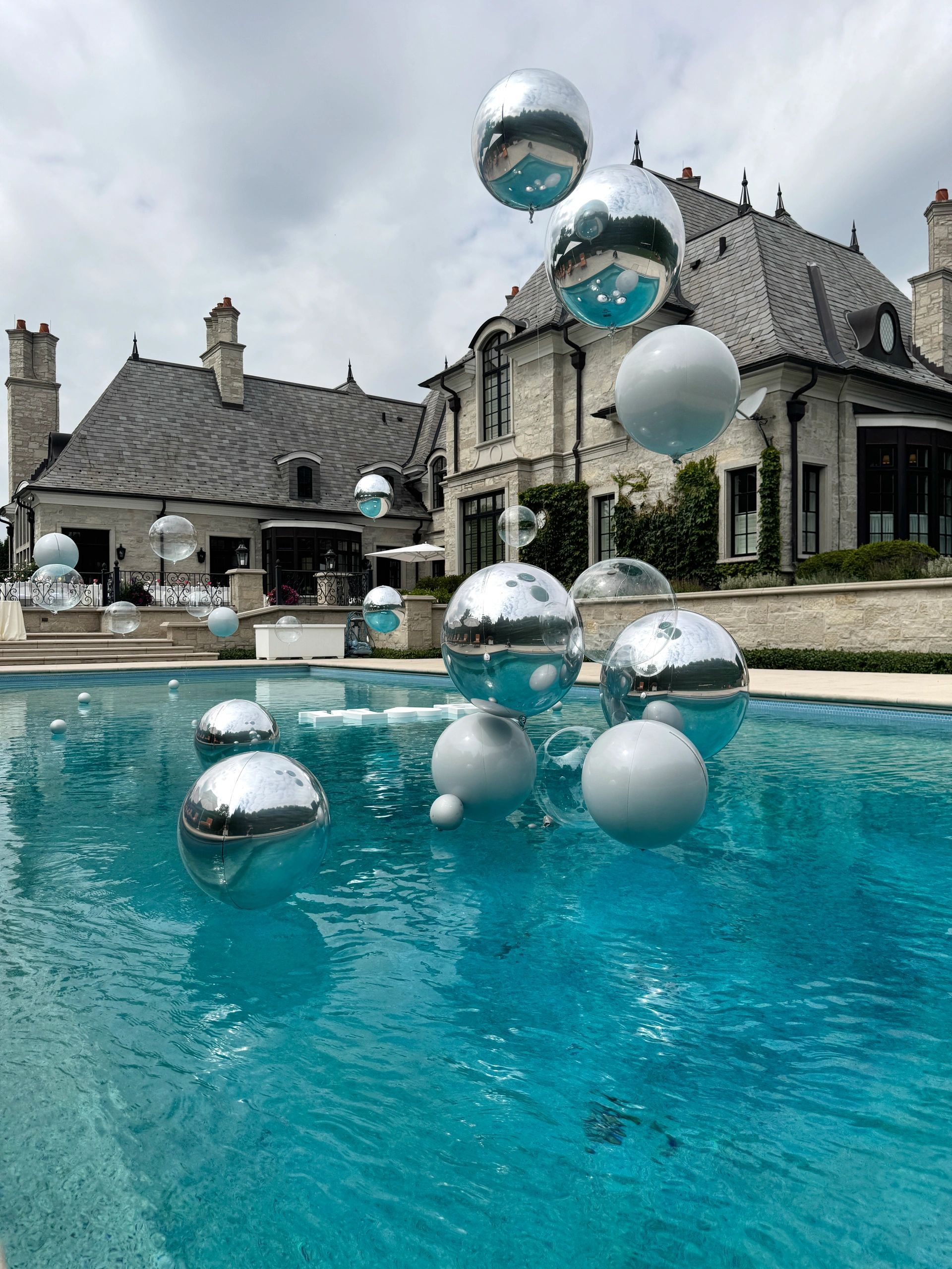 White and silver Orbz and bubble balloons filled with helium, floating above pool.