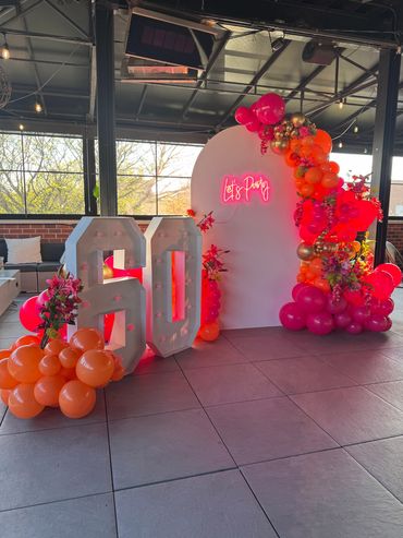 Large birthday backdrop with marquee number 60, florals and pink neon sign "Let's Party".