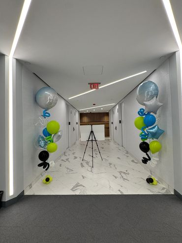 Two helium balloon bouquets with swirl and star and jumbo topper in a white corridor.