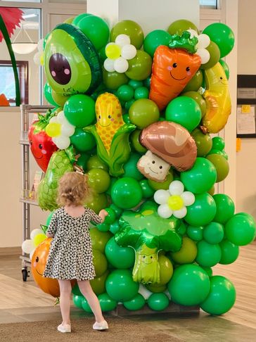 A green balloon wall featuring foil garden symbol balloons and decorative balloon flowers.