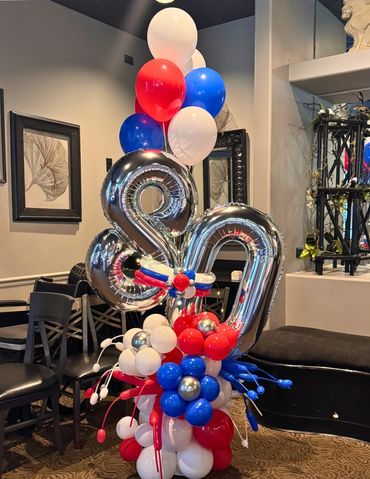 Balloon bouquet with large foil number 80 in USA colors and helium balloons on top.