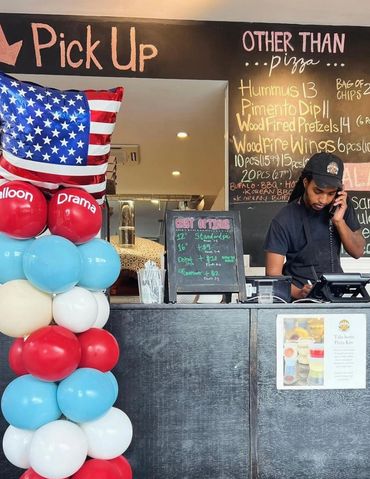 Balloon column displayed at a pizzeria checkout desk with staff taking a phone order. 