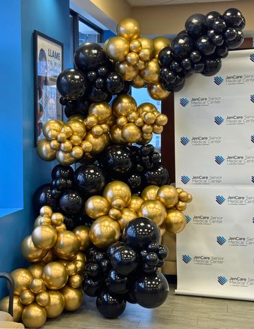 Black and gold luxury balloon garland installed on a company backdrop stand for a corporate event.
