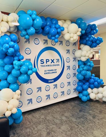 Organic balloon garland surrounding a company banner at a corporate event.