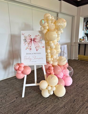 An easel decorated with balloons for a baby shower featuring a welcoming sign in the middle.