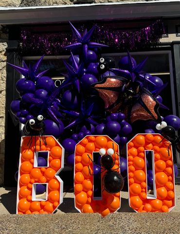 Purple balloon garland with bats and spiders above orange BOO marquee letters.
