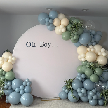 Blue and cream balloons with greenery around a circle backdrop and vinyl sign