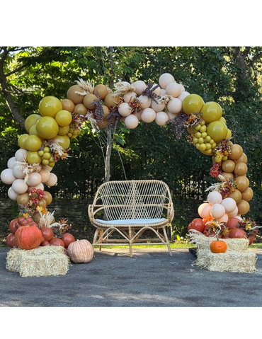 Fall-themed balloon arch with pumpkins and rustic seating.