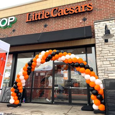 Black, white ,and orange balloon arch installed in front of Little Caesars restaurant.
