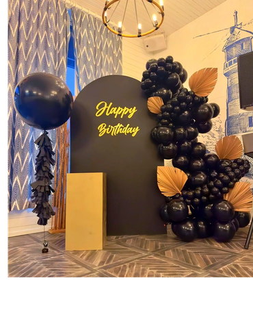 Black birthday backdrop with black balloons, palm leaves, dessert table, and jumbo helium balloon. 