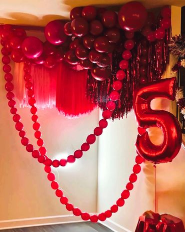 Red ceiling balloons with hanging streamers and helium number five balloon.