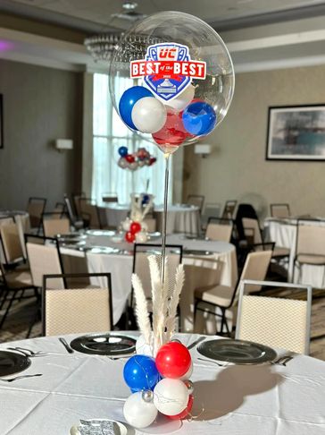 Air-filled balloon centerpiece in American flag color with lights, pampas, and logo topper.