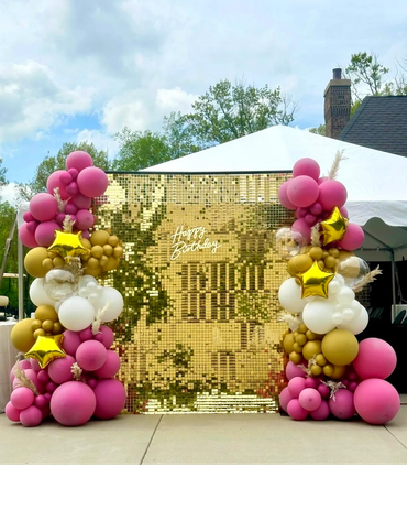 Gold sequin wall with balloon garlands, balloon stars, pampas grass, and neon sign "Happy Birthday".