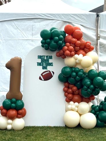 Small backdrop with balloon garland, vinyl sign, and number one balloon column.