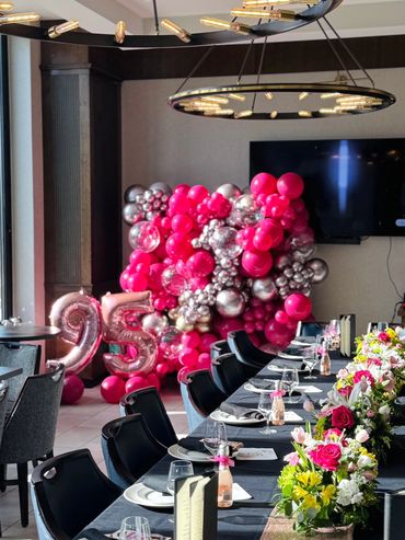 Pink and silver organic balloon wall with foil numbers 95 in a restaurant setting.
